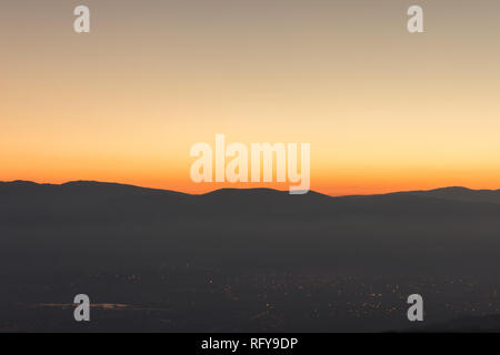 Berg Silhouetten, entsättigt Stadtbild bei Nacht die Lichter und brennenden Sonnenuntergang Himmel Stockfoto