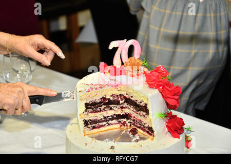 Kuchen Schneiden mit einem Messer zu 70 Geburtstage feiern. Stockfoto