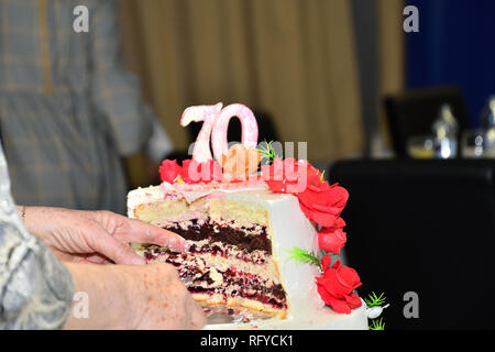Kuchen Schneiden mit einem Messer zu 70 Geburtstage feiern. Stockfoto
