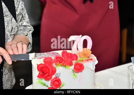 Kuchen Schneiden mit einem Messer zu 70 Geburtstage feiern. Stockfoto