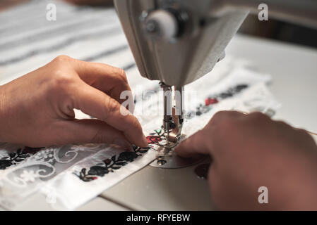 Frau Näherin Hände verbinden weißen Stoff details mit Blumen bunte Stickerei mit Streifen aus Spitze auf moderne, kompakte elektrische Nähmaschine Machin Stockfoto