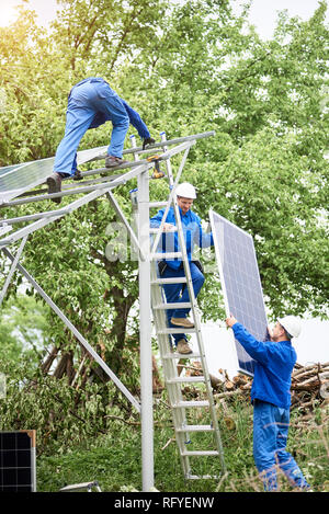 Installieren von stand-alone-Solar Photovoltaik Panel System. Arbeitnehmer in Hard - Hüte und Blau insgesamt heben das Solarmodul auf Metall-Plattform. Alternativ Stockfoto