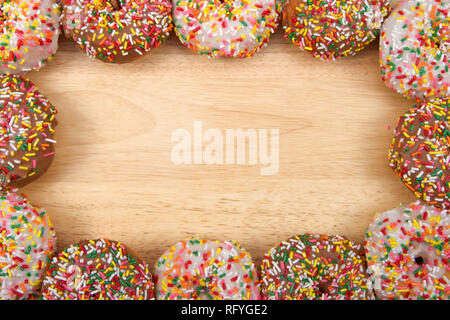 Flach Ansicht vieler frosted Donuts, Schokolade und Vanille mit Süßigkeiten besprüht in einem grenzüberschreitenden Rahmen auf hellem Holz Tisch mit Kopie Raum angeordnet. Stockfoto