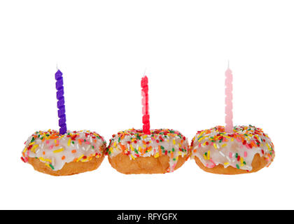 Vanilla cake Donuts mit weißem Zuckerguss und bunten Süßigkeiten besprüht bis Nebeneinander aufgereiht, lila und rosa Kerzen auf weißem Hintergrund. Stockfoto