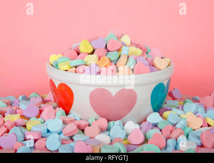 Schüssel mit Herzen holding Haufen Süßigkeiten Herzen durch Haufen von mehr Süßigkeiten auf rosa Hintergrund umgeben. Die traditionellen Valentinstag Süßigkeit. Stockfoto