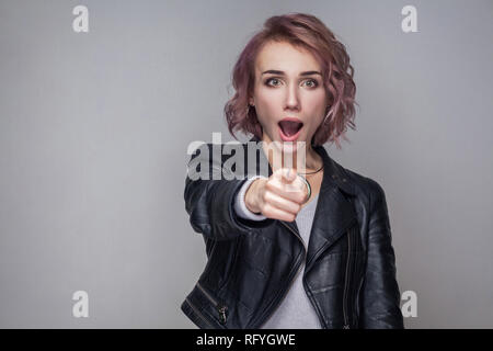 Portrait von überrascht schöne Mädchen mit kurzen Frisur und Make-up in schwarzem Leder Jacke stehen, zeigen und auf Kamera mit entsetzten Gesicht Stockfoto