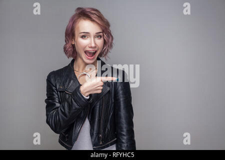 Portrait von überrascht schöne Mädchen mit kurzen Frisur und Make-up im lässigen Stil schwarze Lederjacke stehen, schauen und zeigen auf Copyspace. Stockfoto