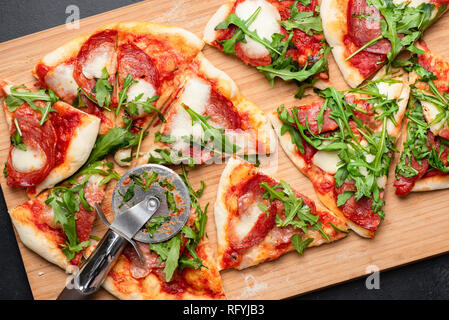 Pizza mit Salami, Mozzarella und Tomaten Sauce garniert mit Rucola. Geschnitten Pizza. Tabelle Ansicht von oben Stockfoto