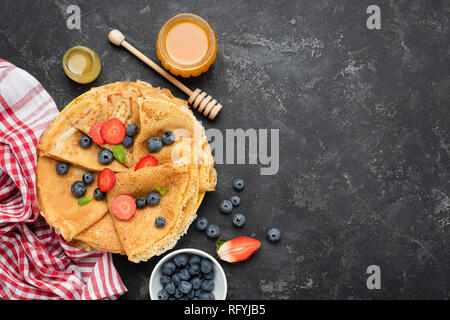 Crepes oder Blini mit frischen Beeren und Honig auf Schwarz konkreten Hintergrund. Ansicht von oben mit der Kopie Platz für Text, Rezept, Menü Stockfoto