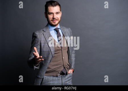 Eine selbstbewusste Elegante hübscher junger Mann, der vor einem grauen Hintergrund in einem Studio trägt einen schönen Anzug. Stockfoto