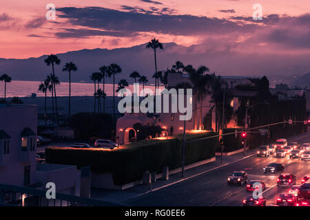 Lila Sonnenuntergang in Santa Monica State Beach mit Schattenrissen von Palmen und Verkehr auf einer pazifischen Freeway Stockfoto