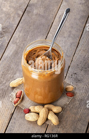 Erdnussbutter im Glas und Löffel auf hölzernen Hintergrund Stockfoto
