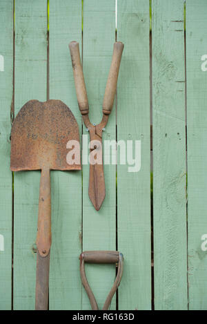 Alte verrostete gardening Tools, einschließlich einer Schaufel und Gartenscheren auf einem Holz Garten Zaun montiert grün lackiert Stockfoto