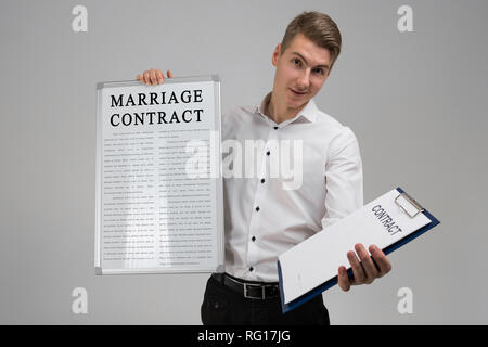 Junger Mann mit Plakat mit Ehe und Vertrag auf hellem Hintergrund isoliert Stockfoto