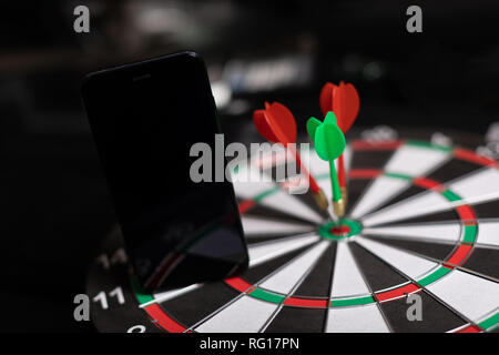 Telefon steht auf Dart Feld mit drei Darts red Ziel in der Nähe des hit-up Stockfoto