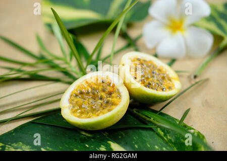 Maracuja Maracuja die Hälfte noch Leben. Exotische saftige Saatgut Passionsfrucht auf grünem Blatt flach mit weißen Blumen. Tropische gesunde organische Foo Stockfoto