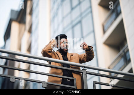 Portrait stattlichen indischen Geschäftsmann auf der Suche smart Watch und im Freien Stadt mit hohen Gebäude Hochhaus Hintergrund schockiert. Stockfoto