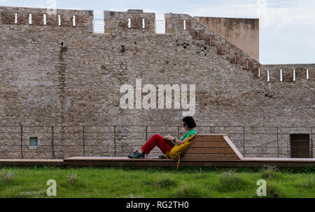 Frau entspannend auf Holzbank, Festung Wand des Castello Maniace im Hintergrund, Syrakus, Sizilien, Italien, Europa Stockfoto