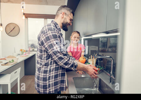 Hohes gut aussehender bärtiger Mann in Brillen waschen Gemüse vor dem Frühstück Stockfoto