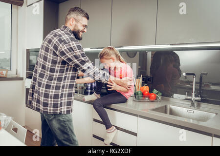 Süße langhaarige Mädchen in einem rosa T-Shirt Spaß mit ihrem Vater in der Küche Stockfoto