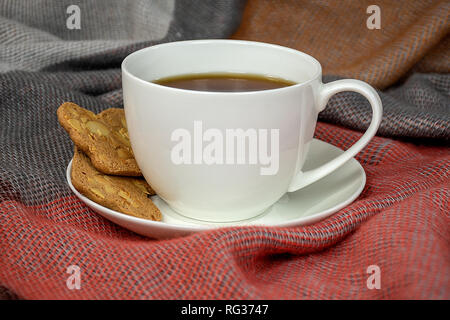 Nahaufnahme der schwarzen Kaffee in weiße Tasse mit Untertasse mit Plätzchen und warmen Decke Stockfoto