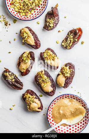 Termine gefüllt mit Erdnussbutter und Pistazien auf einem weißen Hintergrund. Gesunde vegane Ernährung Konzept. Stockfoto