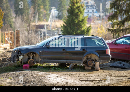 Rotes Auto in Freizeit und alten rostigen gebrochen Papierkorb Auto nach einem Crash Unfall ohne Räder auf Holz Stempel an einem sonnigen Tag im Freien auf Abgebrochen Stockfoto