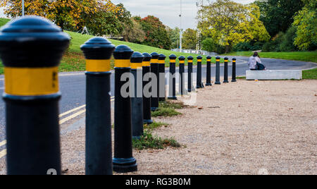 Frau auf konkrete Sitzbank neben der Straße sitzen, Reihe der Poller im Vordergrund, Rückansicht, Crystal Palace, London, England, Großbritannien Stockfoto