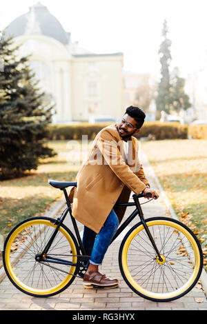 Seitenansicht eines indischen hipster Mann im Mantel zu Fuß mit dem Fahrrad auf einer Straße der Stadt Stockfoto