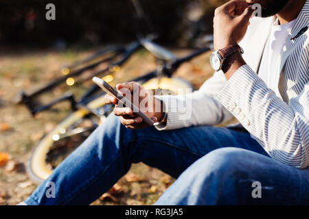 Der Mensch mit seinem Handy outdoor, ganz nah. Handy in die Hände einer jungen hipster Mann mit Fahrrad auf dem Hintergrund des grünen Grases. Stockfoto