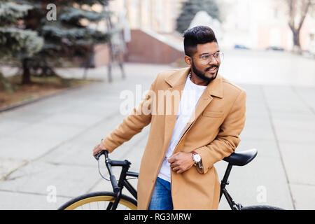 Portrait von indischen Hipster bärtiger Mann mit dem braunen Haar zu Fuß mit dem Fahrrad auf der Straße Stockfoto