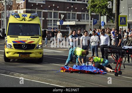 Blick auf eine junge weibliche Opfer liegen auf der Straßenbahn nach einem Unfall, der von einem Krankenwagen Auto umgeben, Krankenwagen Mitarbeiter und Passanten. Stockfoto