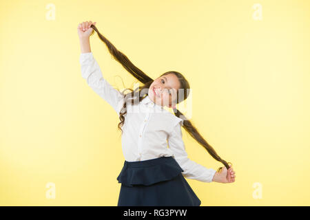 Deal mit langem Haar frisur. Kid girl langen pferdeschwanz Frisur. Kind Schuluniform machen Frisur. Kid stilvolle modischen posieren Pferdeschwänze halten Frisur. Komfortable und einfache Frisur. Stockfoto