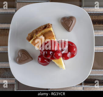 Flach von Cherry Cheesecake mit zwei Schokolade Herzen auf einem braunen Fliesen- Hintergrund. Stockfoto