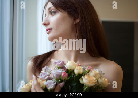 Schöne glückliche Frau am Fenster aus dem Schlafzimmer mit einem Blumenstrauß. Feder Konzept Stockfoto