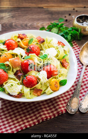 Fettuccine Pasta mit gebackenen Tomaten, Schinken und Mozzarella auf rustikalen Holzmöbeln Hintergrund. Stockfoto