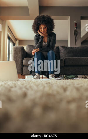 Low Angle View der afrikanischen Frauen sitzen auf der Couch in die Dokumente liegen auf dem Boden mit einem Laptop. Frau arbeitet an einem von zu Hause aus. Stockfoto