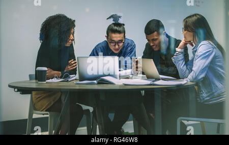 Multiethnische Gruppe junger Studenten studieren. Junge Leute am Tisch sitzen mit Handys beim Studieren. Stockfoto