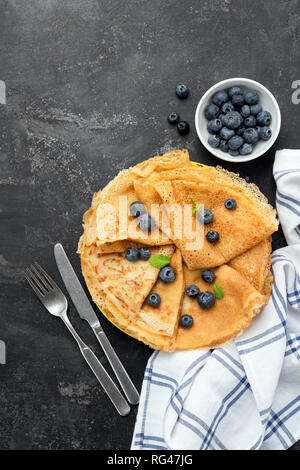 Blini, plinse oder Crepes auf schwarzen Hintergrund mit frischen Blaubeeren serviert. Table Top anzeigen, kopieren Platz für Text, Rezept, Menü Stockfoto