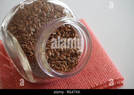 Leinsamen in kleinen Glas Glas auf der Leinwand in lebende Koralle Farbe Ton Stockfoto