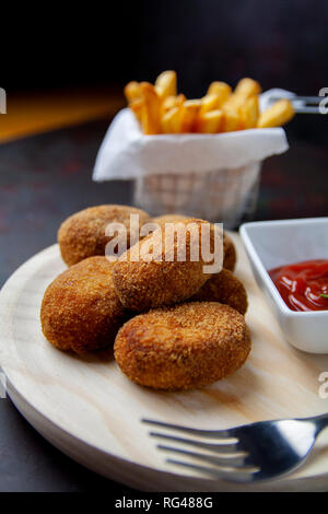 Kroketten mit gebratenen Tomaten/Paradeiser und Chips und dunklen Hintergrund Stockfoto