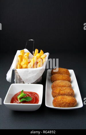 Gourmet Schinken und Hähnchen Kroketten mit gebratenen Tomaten/Paradeiser und Chips auf dunklem Hintergrund Stockfoto