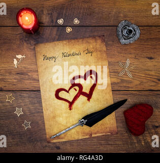 Classic Happy Valentinstag Karte Hand auf Pergament rot bemalten Herzen rote Kerze Dekorationen silber Feder geschrieben und auf Vintage oak Ansicht von oben stehen Stockfoto