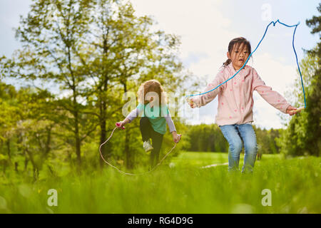 Zwei Mädchen im Seilspringen auf einer Wiese im Park im Sommer Ferien Stockfoto