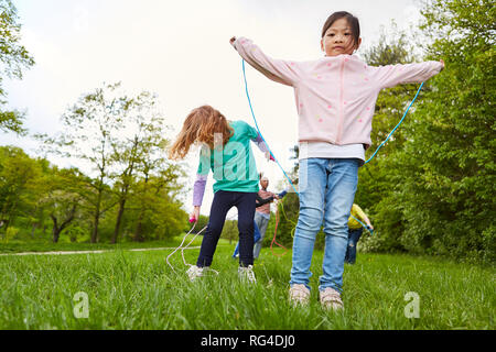 Kinder im Kindergarten zusammen beim springen Seil auf einer Wiese im Sommer Stockfoto