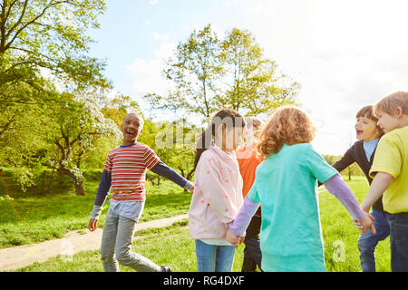 Glückliche Kinder machen eine kreisförmige Tanzen im Park und feiern den Geburtstag Kinder Stockfoto