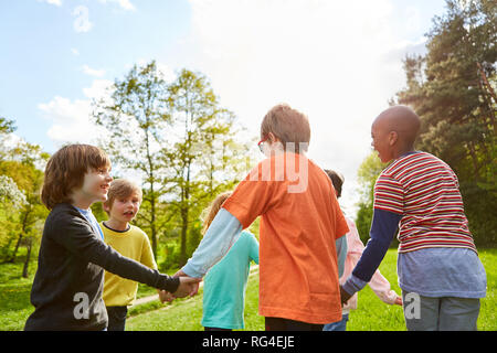 Kinder halten Sie Hände und Tanz im Kreise im Sommer im Park Stockfoto