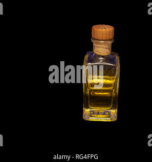 Transparent rechteckige Glas Flasche mit einem Korken verschlossen. Zur Hälfte gefüllt mit einer leuchtend gelbe Flüssigkeit, vor einem schwarzen Hintergrund ausgesetzt. Stockfoto