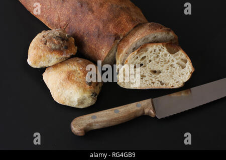 Nur mit Sauerteig gebacken, hausgemachtes Brot und Brötchen mit Samen - Rustic mit Messer durch Scheiben Brot liegen. Schönen malerischen Bild auf Schwarz bac Stockfoto