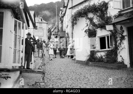 Touristen, die einen Spaziergang entlang der gepflasterten Straßen von Clovelly, Devon, ca. 1920. Stockfoto